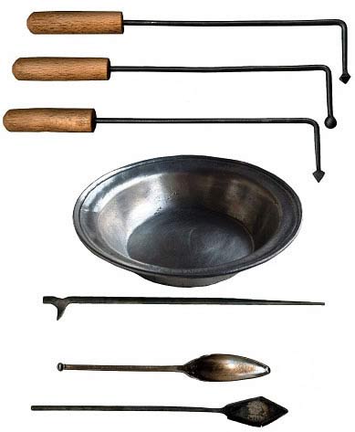 A photo of a collection of several medical instruments from the era of pre-modern or early modern medicine, arranged vertically on a white background. At the top are three iron rods with wooden handles and differently shaped tips, possibly for cauterizing or probing. Below is a metal basin, likely used to catch blood or other fluids during procedures. Underneath are various metal tools, including a long slender hook, a scoop-like spoon, and a flat, diamond-shaped spatula. These instruments suggest use in historical practices like bloodletting, cautery, or rudimentary surgery.