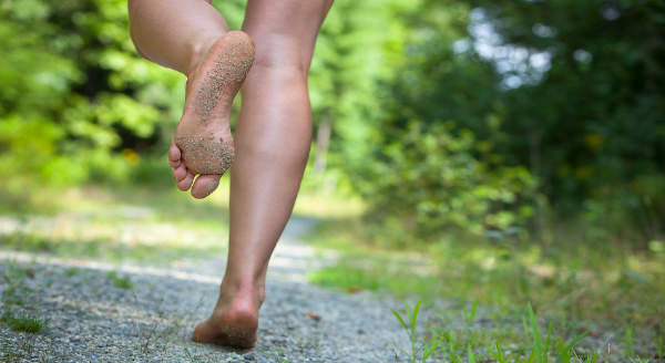 Photograph of the lower legs and feet of someone barefoot running on a gravel trail.