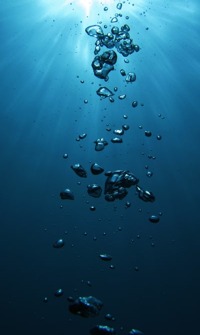 Underwater photo of beautiful deep blue water penetrated by sunbeams, with a column of shiny bubbles.