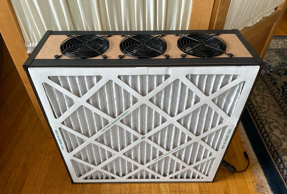 Photo of a Corsi-Rosenthal box with PC fans. It’s the overall shape of a box fan, but instead of one big fan with a rim, there is a row of PC fans mounted on the top, and the front is a big filter.