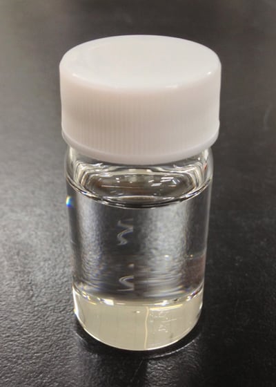 Clear glass vial filled with a transparent liquid, placed on a dark, flat surface.