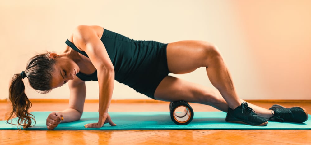 Photograph of a woman using a foam roller on the side of her hip and thigh, a popular method of self-massage.
