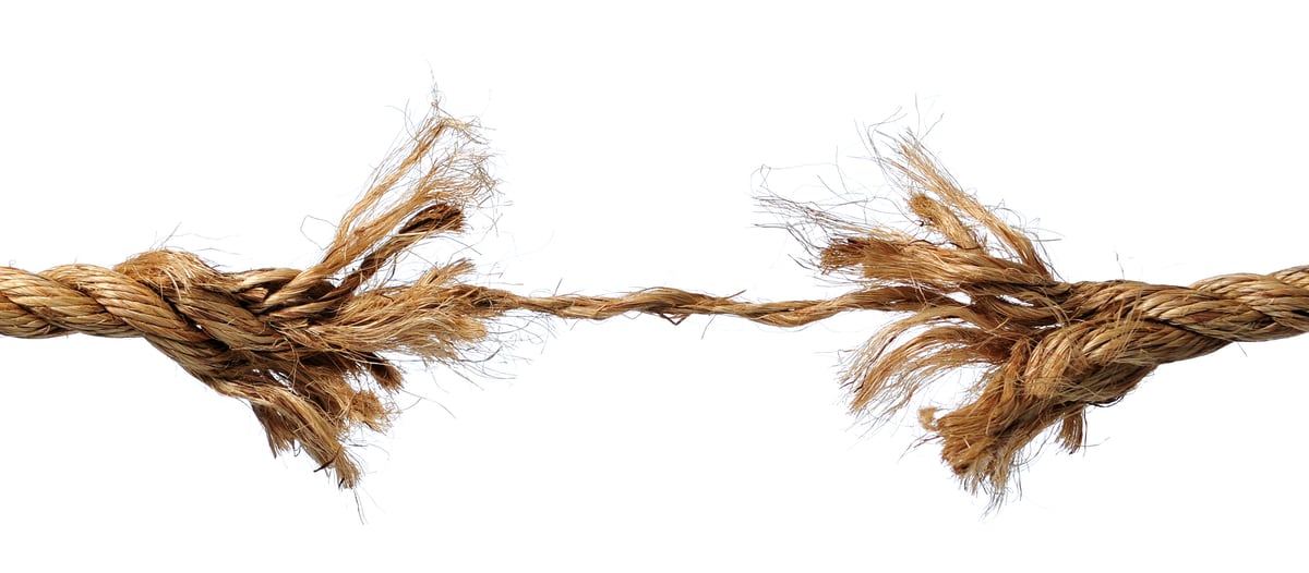 Close-up of a twisted natural fiber rope stretched to its breaking point, with individual strands visibly fraying and separating at two points along its length.