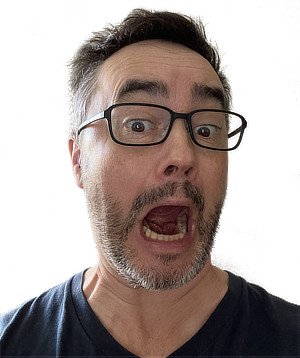 A photo of Paul Ingraham, the author of this post, a middle-aged man with light skin, short dark hair, and a beard, wearing black-framed glasses and a dark-colored T-shirt. He has an exaggerated expression of surprise or shock, with his mouth wide open and eyes wide.