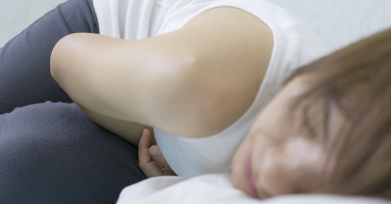 Photo of a woman lying on her side in pain, holding her abdomen.