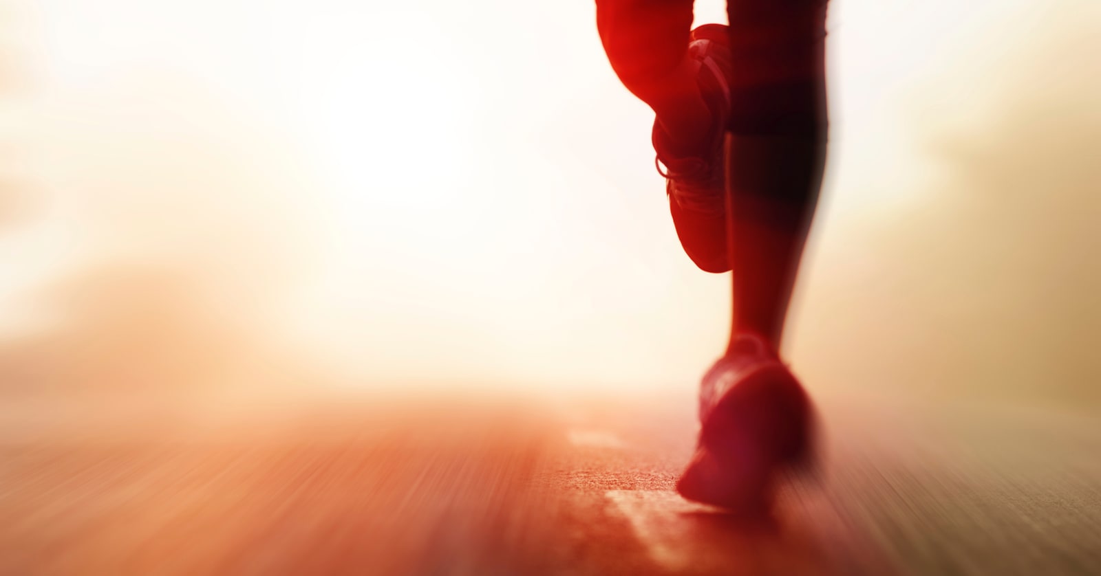 Bright, blurry, warm-toned photo of legs running on pavement.