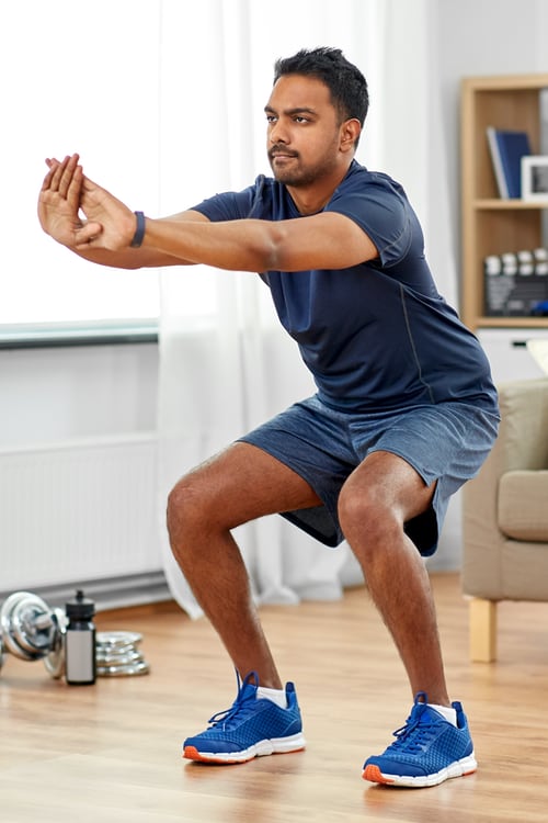 Photo of a man doing a squat exercise in his living room.