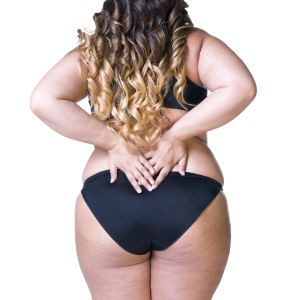 Back view of a slightly overweight woman in a black 2-piece swimsuit, holding her back because she has back pain.