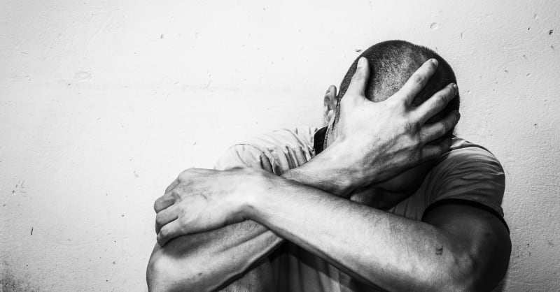 Moody B&W photo of a man holding his head in mental and/or physical pain.
