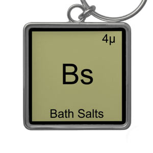 An odd square pendant with a metal rim and the letters “Bs” on an olive green background, with the text “bath salts” in smaller print under that.