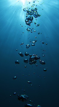 Underwater photo of beautiful deep blue water penetrated by sunbeams, with a column of shiny bubbles.