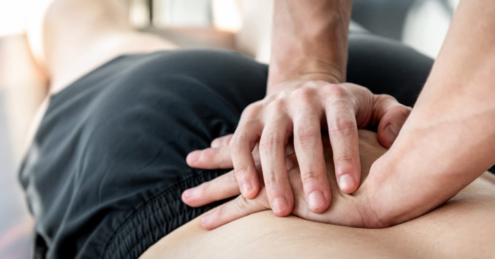 Photo of a pair of hands pressing down on a man’s lower back, suggesting chiropractic treatment.
