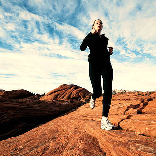 Photo of a woman running outdoors in a spectacular uneven terrain of red rock.--cap:ITBS symptoms are most likely to crop up while going down—so trail runners and hikers are at the greatest risk.