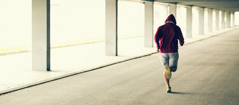 Photo of a male runner with shin splints, jogging away from the camera in a brightly sunlit empty garage.