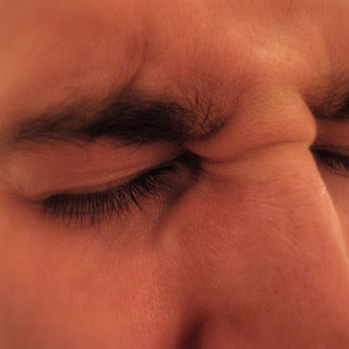 Photographic closeup of a man’s squinting face, implying a severe headache.