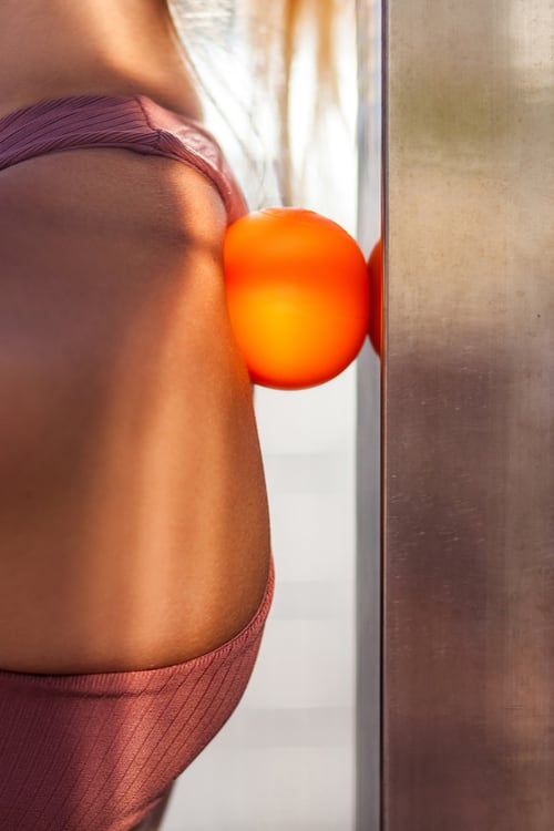 Close-up photo of a woman’s upper back with a massage ball trapped between her back and a wall or post.