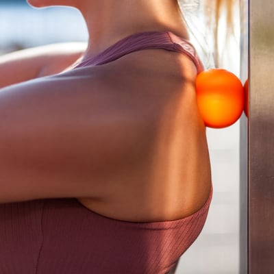 Close-up photo of a woman’s upper back with a massage ball trapped between her back and a wall or post.