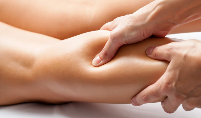 Landscape photo, close up, bright, of hands massaging a woman’s calf.