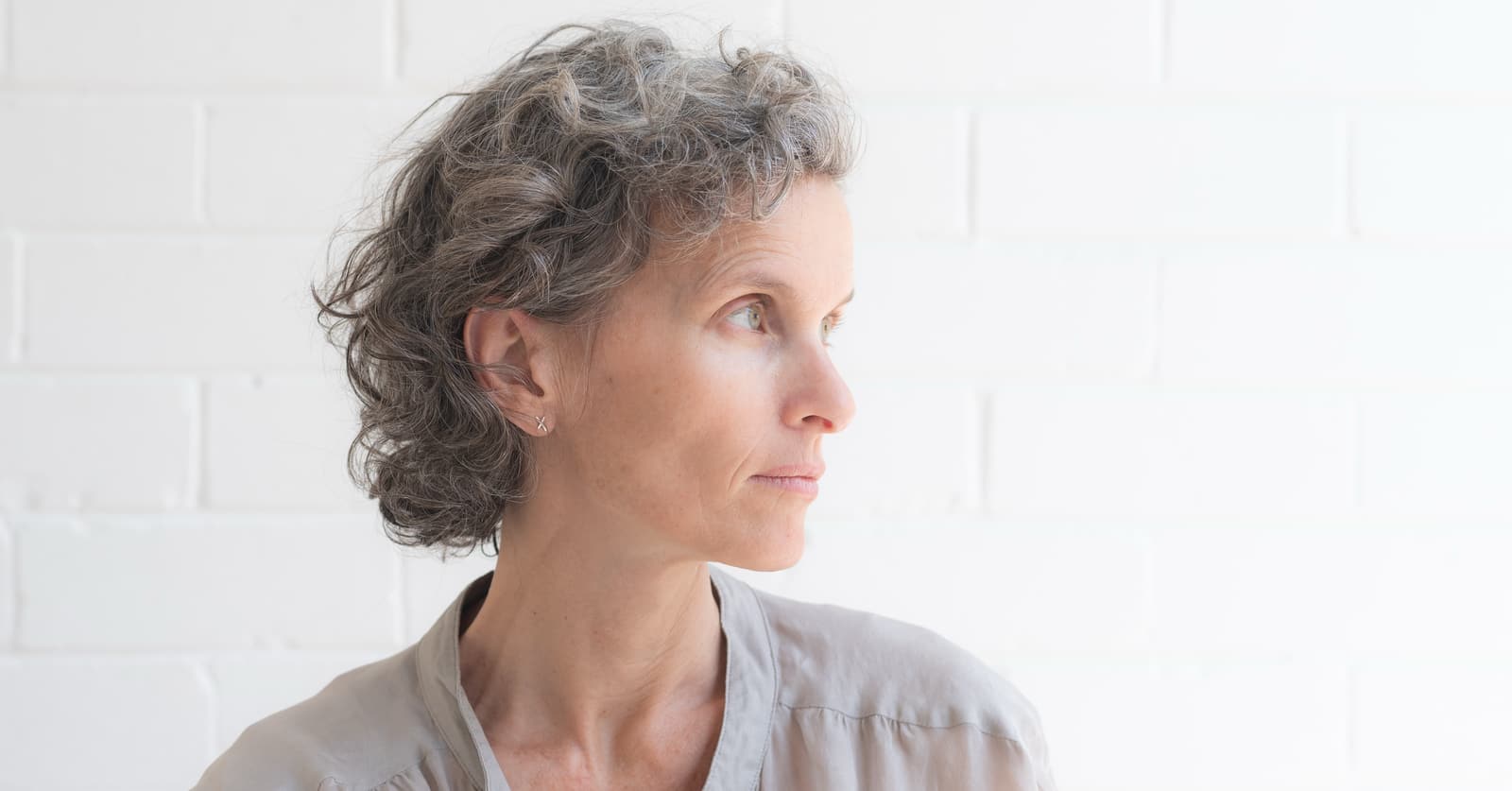 Nice stock photo of an older woman in front of a white brick wall staring thoughtfully at nothing in particular.