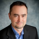 Head shot of author Paul Ingraham, handsome devil, tidy dark hair, thick eyebrows, and a short goatee, in a black suit jacket and a nice blue shirt.