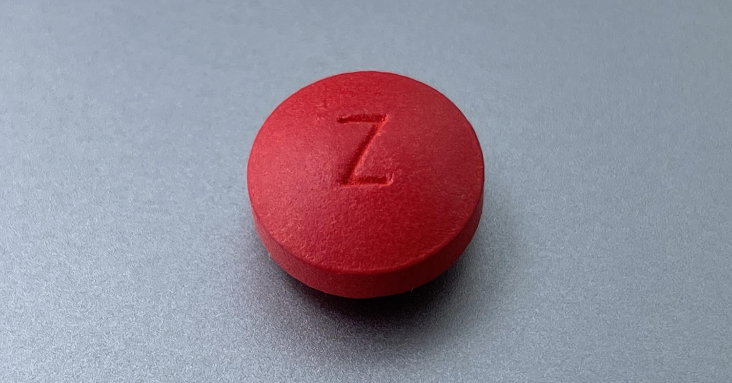 Closeup photograph of a bright red acetaminophen pill on a smooth metal surface.