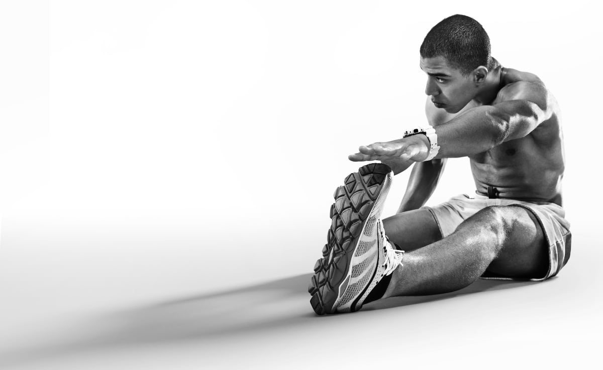 B&W photo of a fit topless man in athletic wear reaching for his toes.
