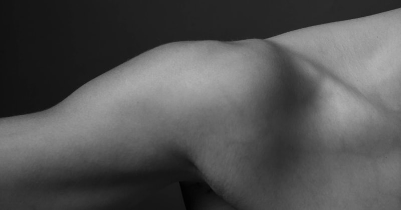 B&W photo of a woman’s shoulder, upper arm, and upper chest.