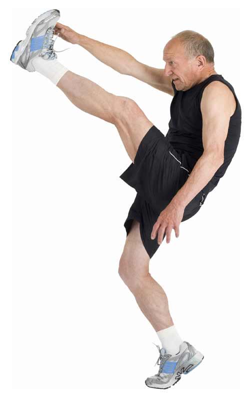 Photo of an elderly man standing on one leg, kicking the other up high to his hand. He looks like he’s trying really hard.
