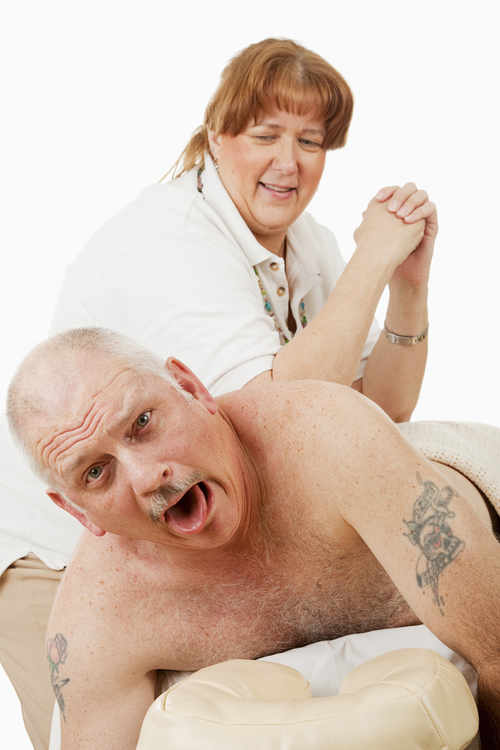 Photograph of a man receiving a painful deep tissue massage from a sterotyped stocky female massage therapist.