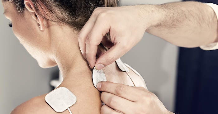 Photograph of a man applying TENS electrodes to a woman’s upper back.
