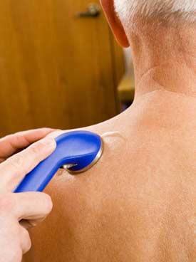 Photograph of ultrasound applied to the back of an elderly man’s shoulder.