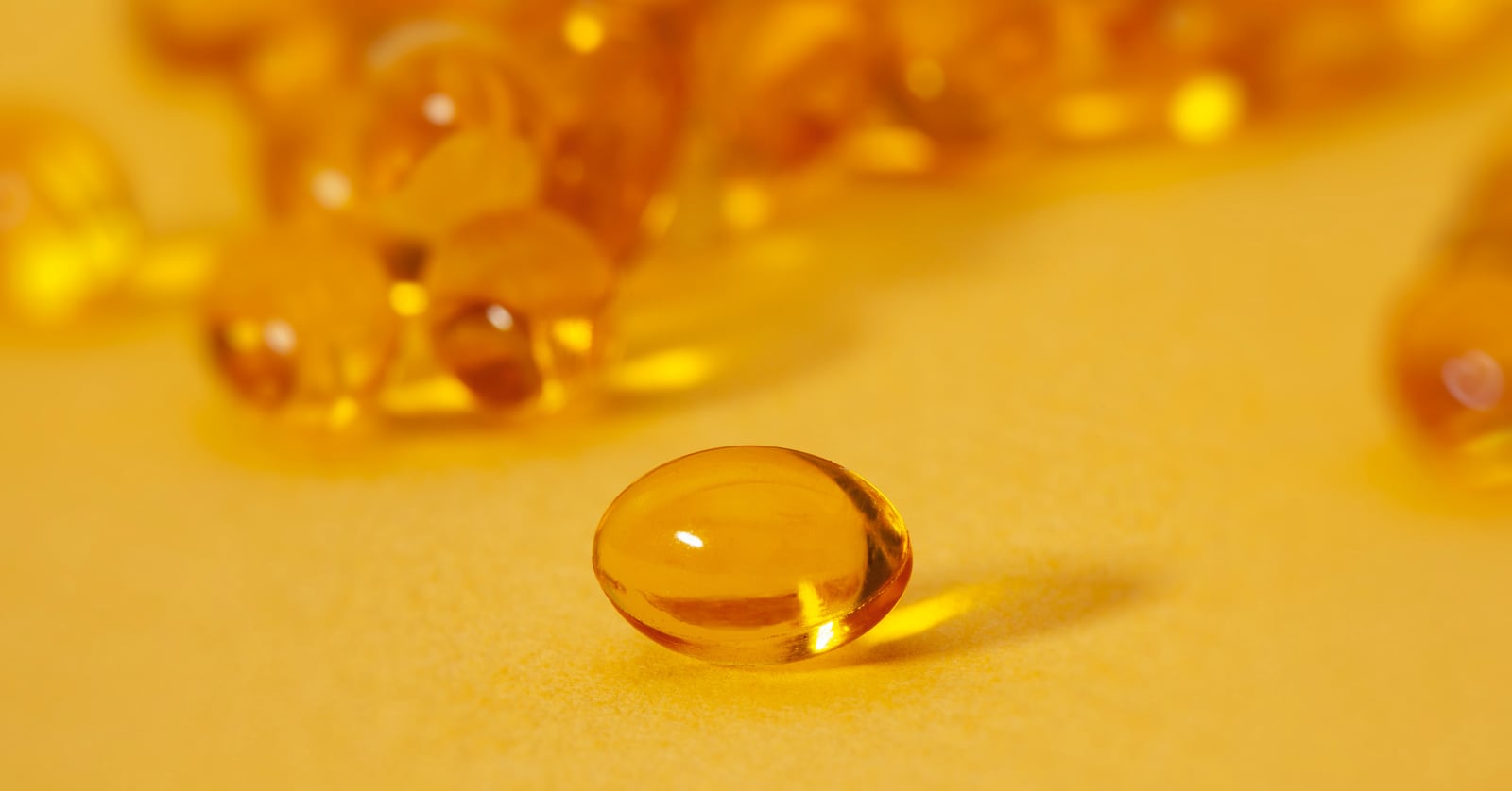 Photograph of shiny, brightly lit vitamin D gel capsules close up.